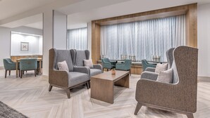 A modern hotel lobby with grey upholstered armchairs, a wooden coffee table, and a large window with sheer curtains. - Staybridge Suites Port Arthur by IHG (Port Arthur)