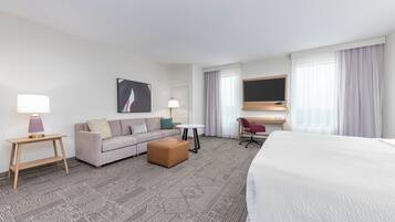 Quarto de hotel com cama, sofá, escrivaninha, cadeira, mesinha e abajur.