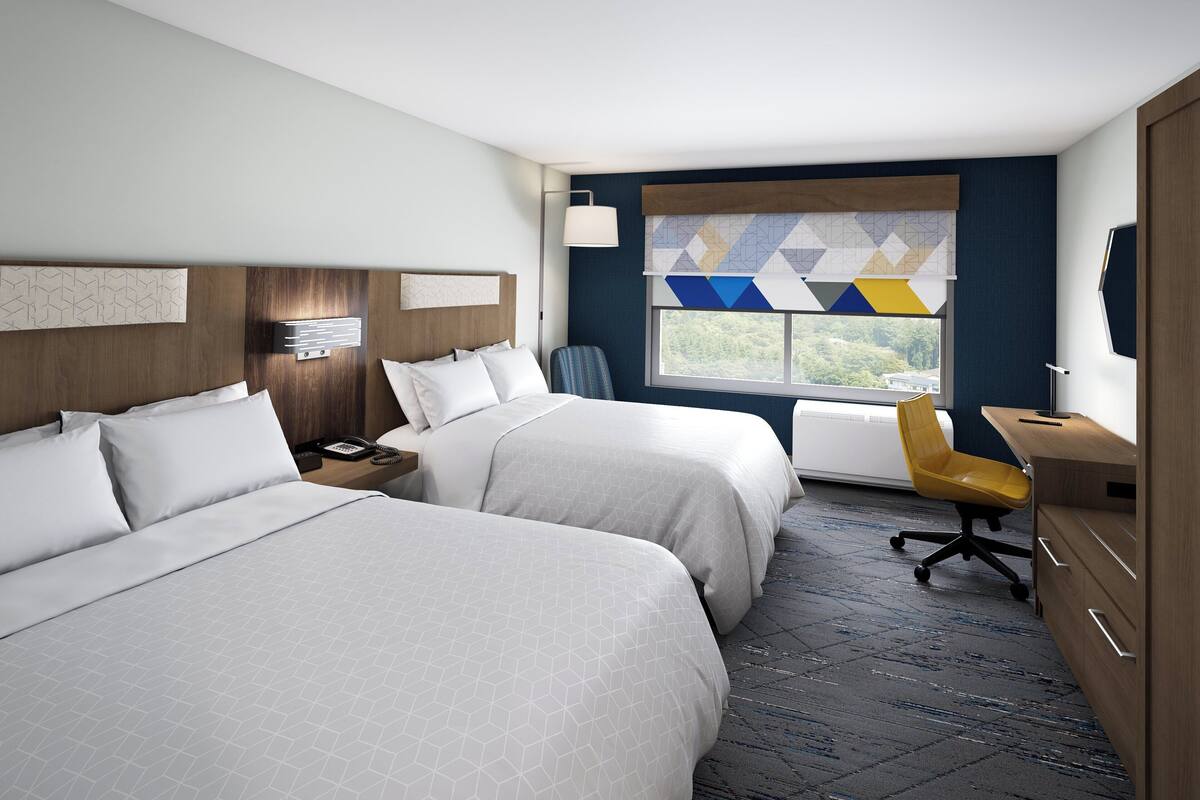 A hotel room with two beds, a desk, a chair, and a window with a view.