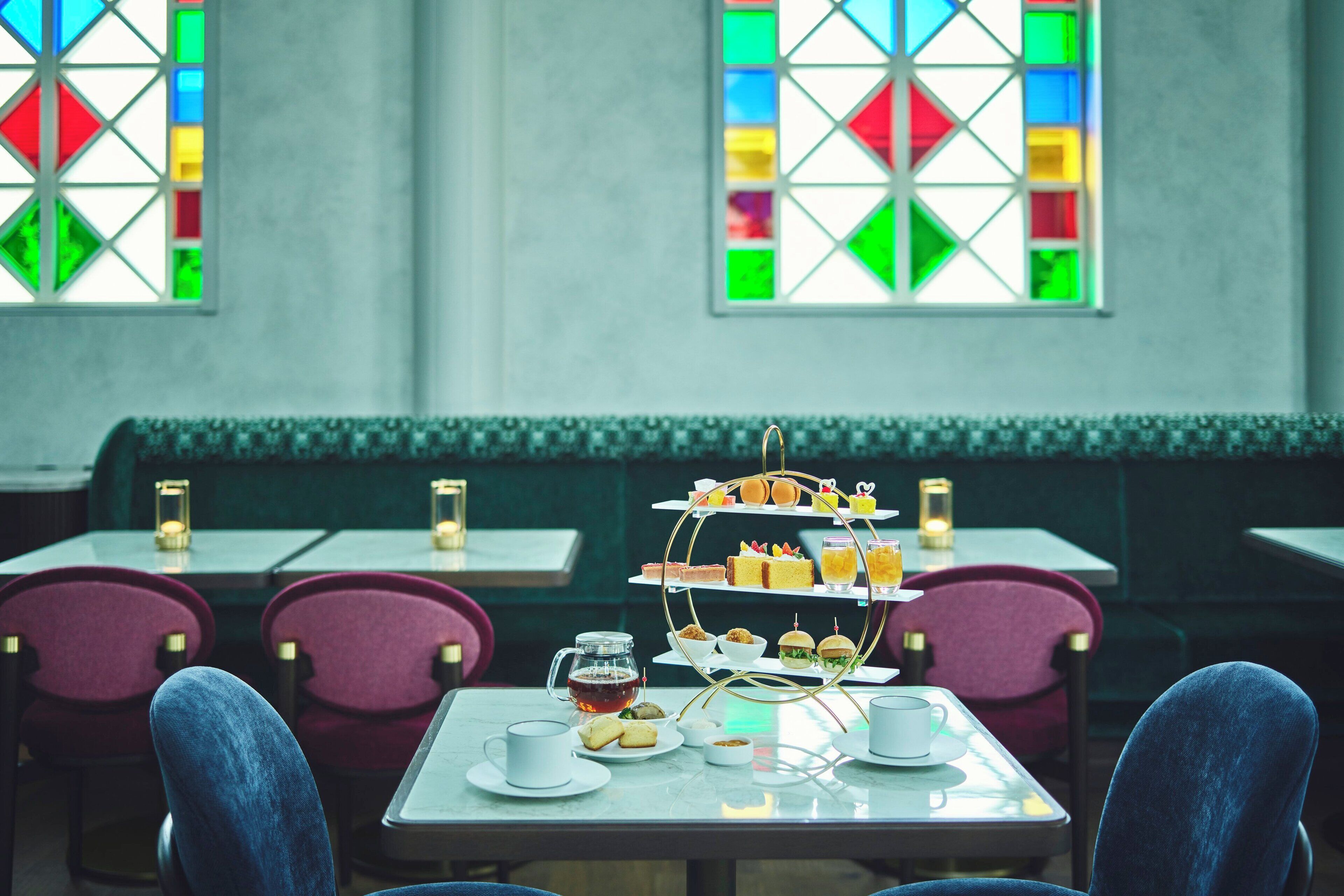 Een eethoek met een dessertetage, tafels, stoelen en een glas-in-loodraam.