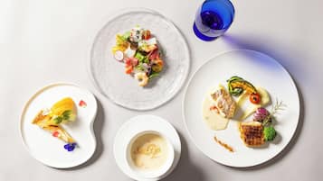 A table with three plates of food, a glass of blue liquid, and a small bowl of soup.