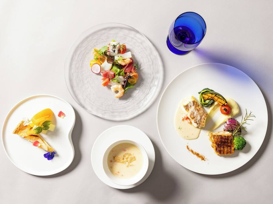 A table with three plates of food, a glass of blue liquid, and a small bowl of soup.