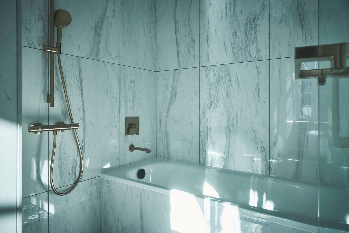 A modern bathroom with a marble wall, a bathtub, and a shower system.