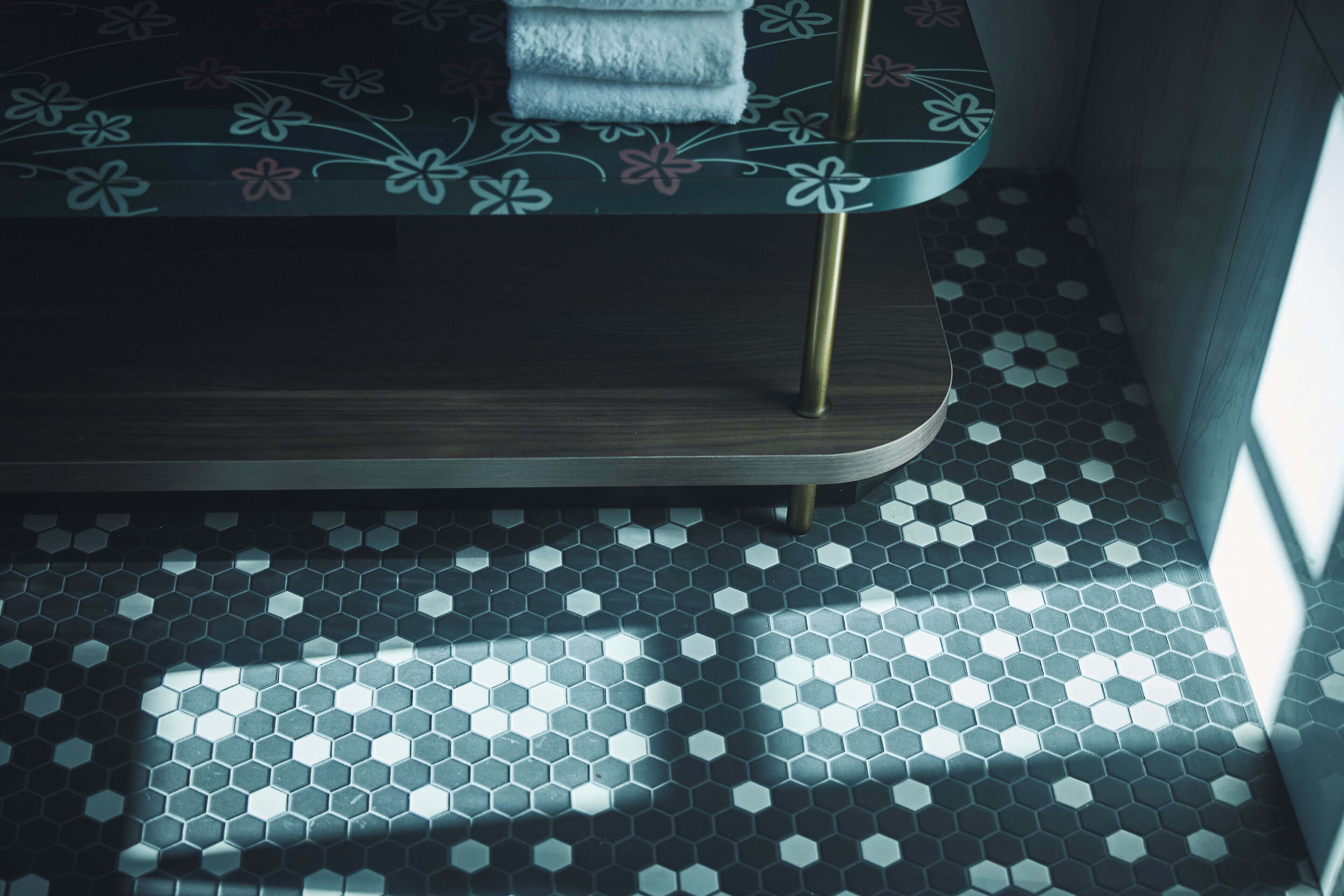 A bed with a floral pattern, a wooden headboard, and a hexagonal tile floor.