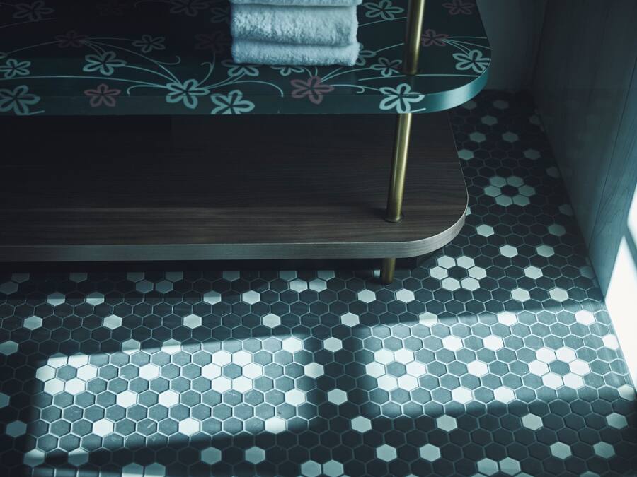 A bed with a floral pattern, a wooden headboard, and a hexagonal tile floor.