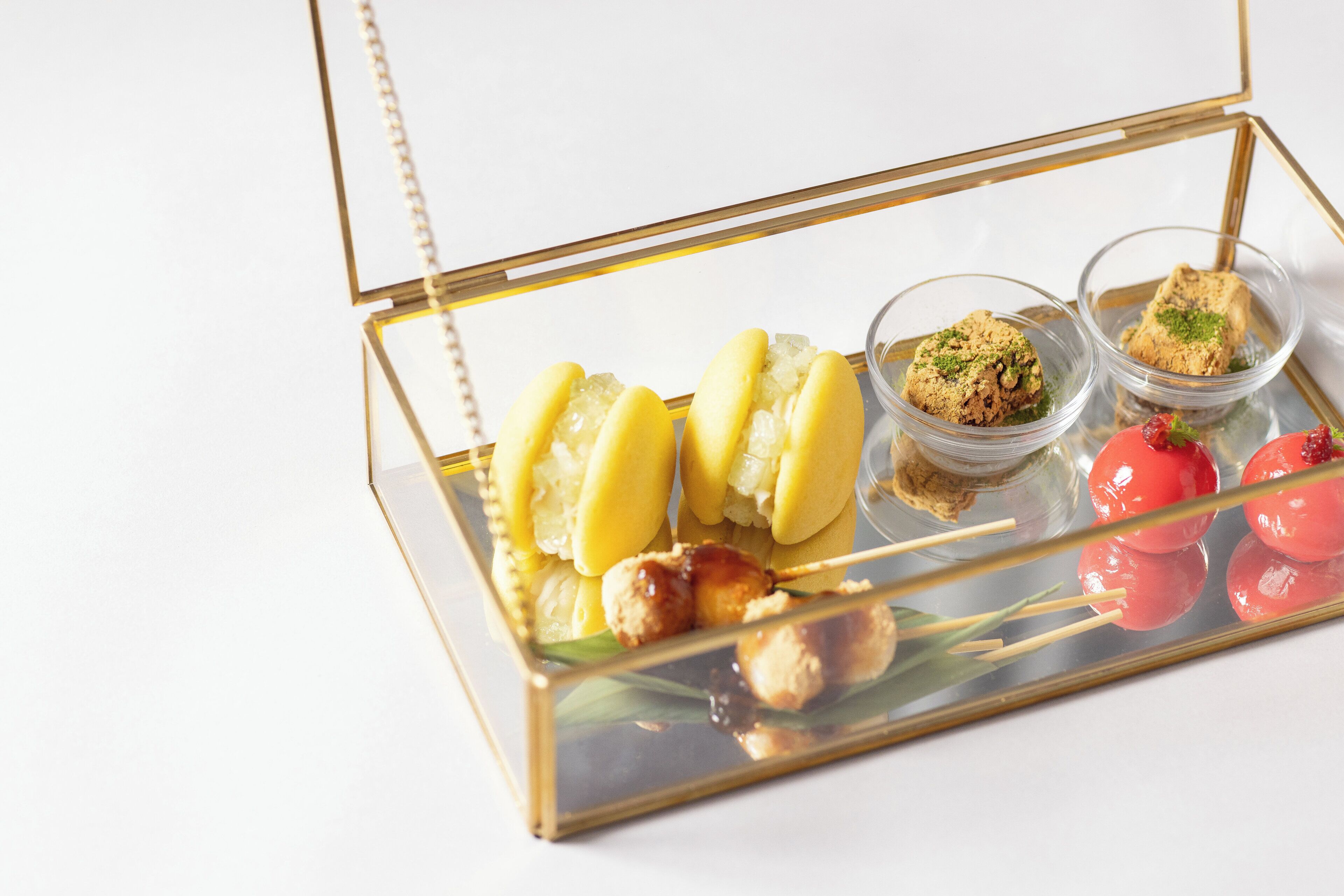 Een glazen displayvitrine met diverse etenswaren, waaronder satéprikkers, een dessert en kleine bakjes.