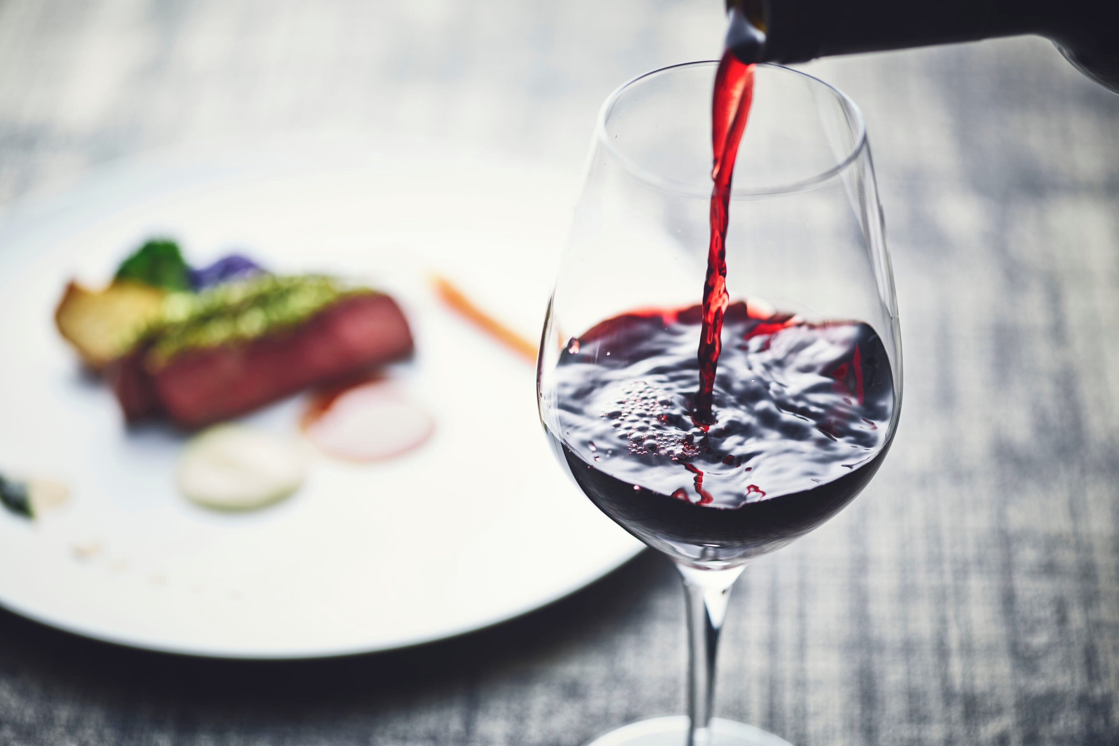 A glass of red wine being poured onto a plate with food.