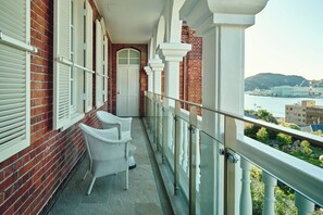 A balcony with white wicker chairs, a white door, and a view of a body of water and buildings. - Hotel Indigo Nagasaki Glover Street by IHG (Nagasaki)
