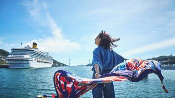 A person holding a colorful kite by the water with a cruise ship in the background.
