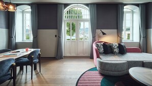 A modern living room with a sofa, a dining table with chairs, and a large window with curtains. - Hotel Indigo Nagasaki Glover Street by IHG (Nagasaki)