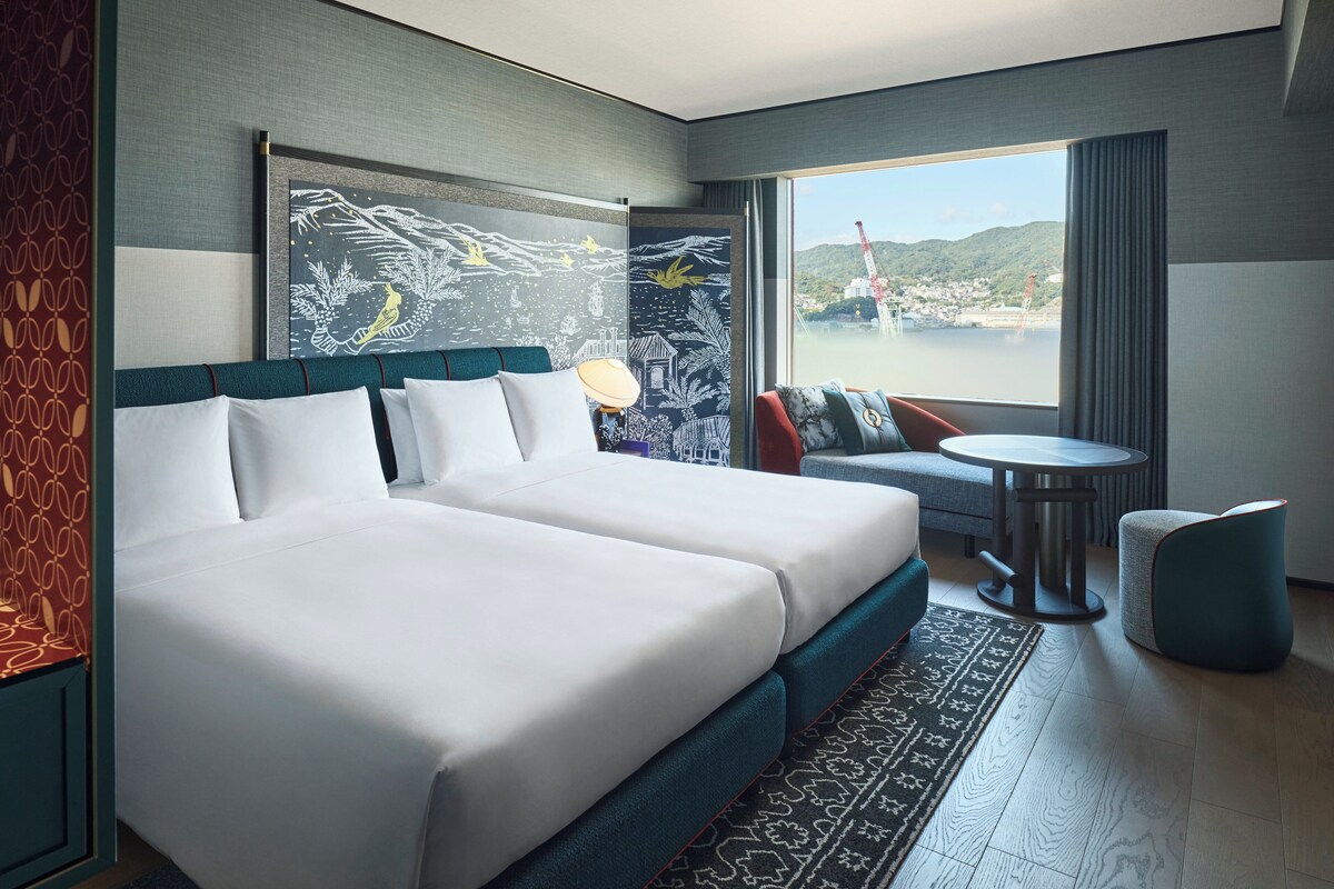 A hotel room with a large bed, a small table, a chair, and a view of a body of water.