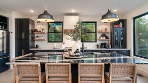 Une cuisine moderne dotée d’un grand îlot central, de meubles de couleur noire et de luminaires suspendus.
