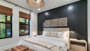 Une chambre moderne avec un grand lit, une table de chevet, un luminaire fixé au mur et une vue sur la verdure.