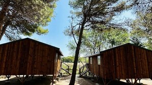 Two wooden cabins with metal supports, surrounded by trees and a clear sky. - Camping 3 étoiles - Piscine  - eehdba (Portel-des-Corbières)