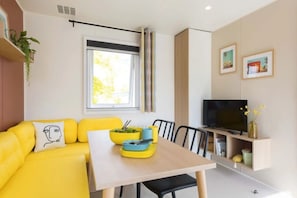 A modern living space with a yellow sofa, a dining table, a TV, and a window with curtains.