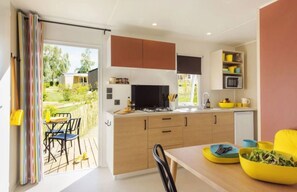 A modern kitchen with a dining area, a view of the garden, and a small refrigerator. - Camping 3 étoiles - Piscine  - eehdba (Portel-des-Corbières)