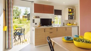 A modern kitchen with a dining area, a view of the garden, and a small refrigerator. - Camping 3 étoiles - Piscine  - eehdba (Portel-des-Corbières)