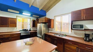 Una cocina con armarios de madera, un refrigerador de acero inoxidable, un microondas y un ventanal amplio.