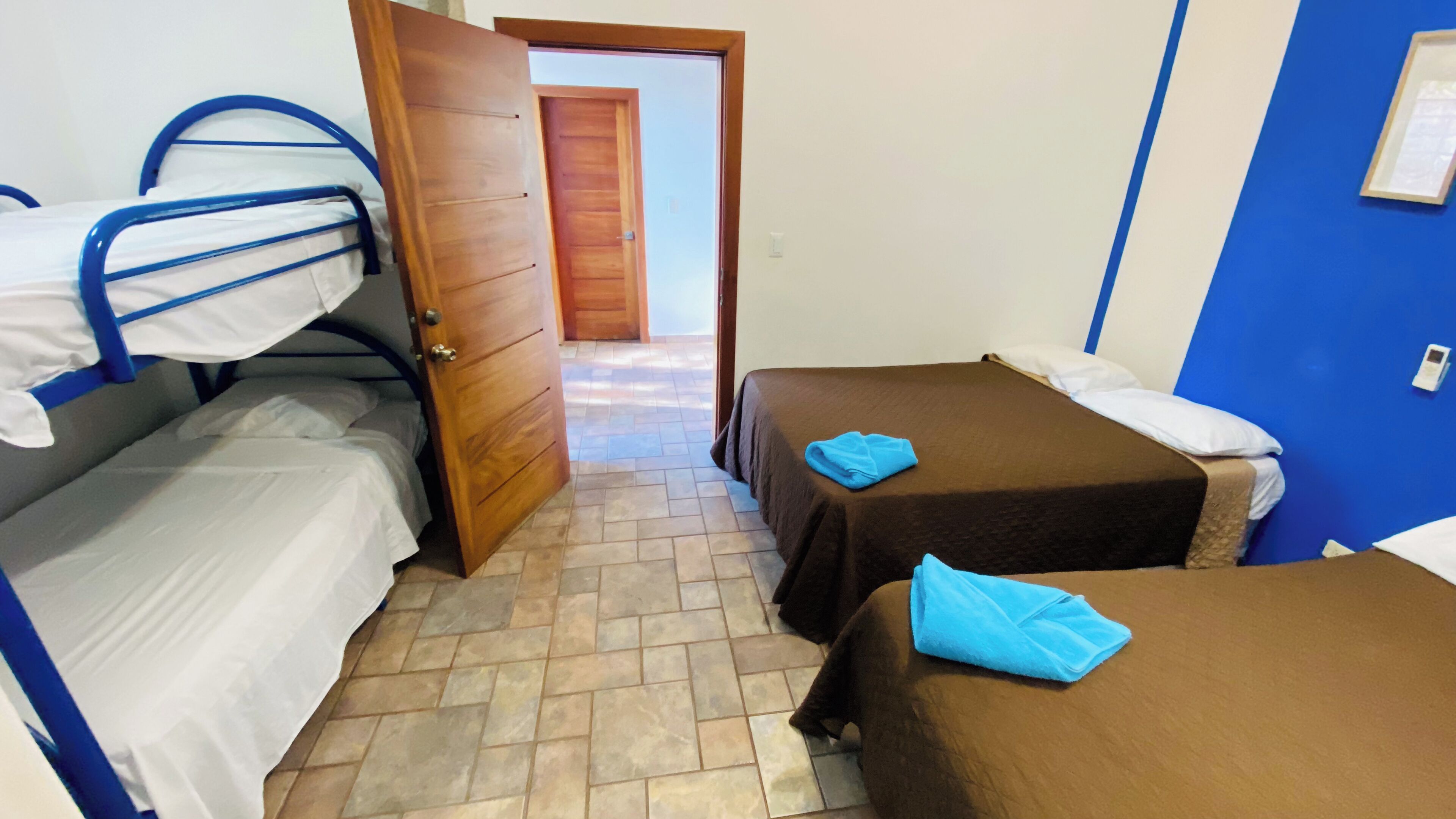 A dormitory room with bunk beds, a wooden door, a tiled floor, and a blue wall.