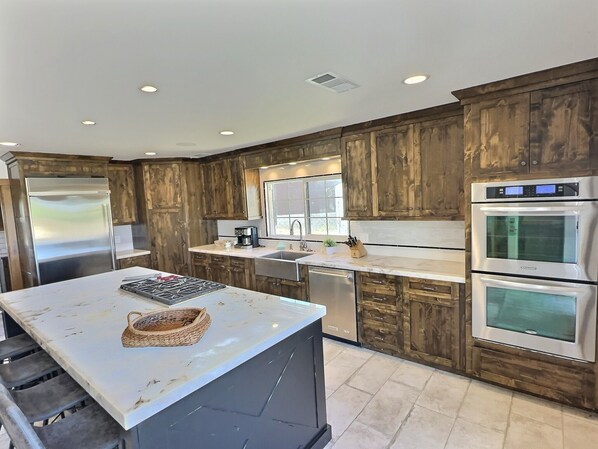 A modern kitchen with wooden cabinetry, stainless steel appliances, and a marble countertop.
