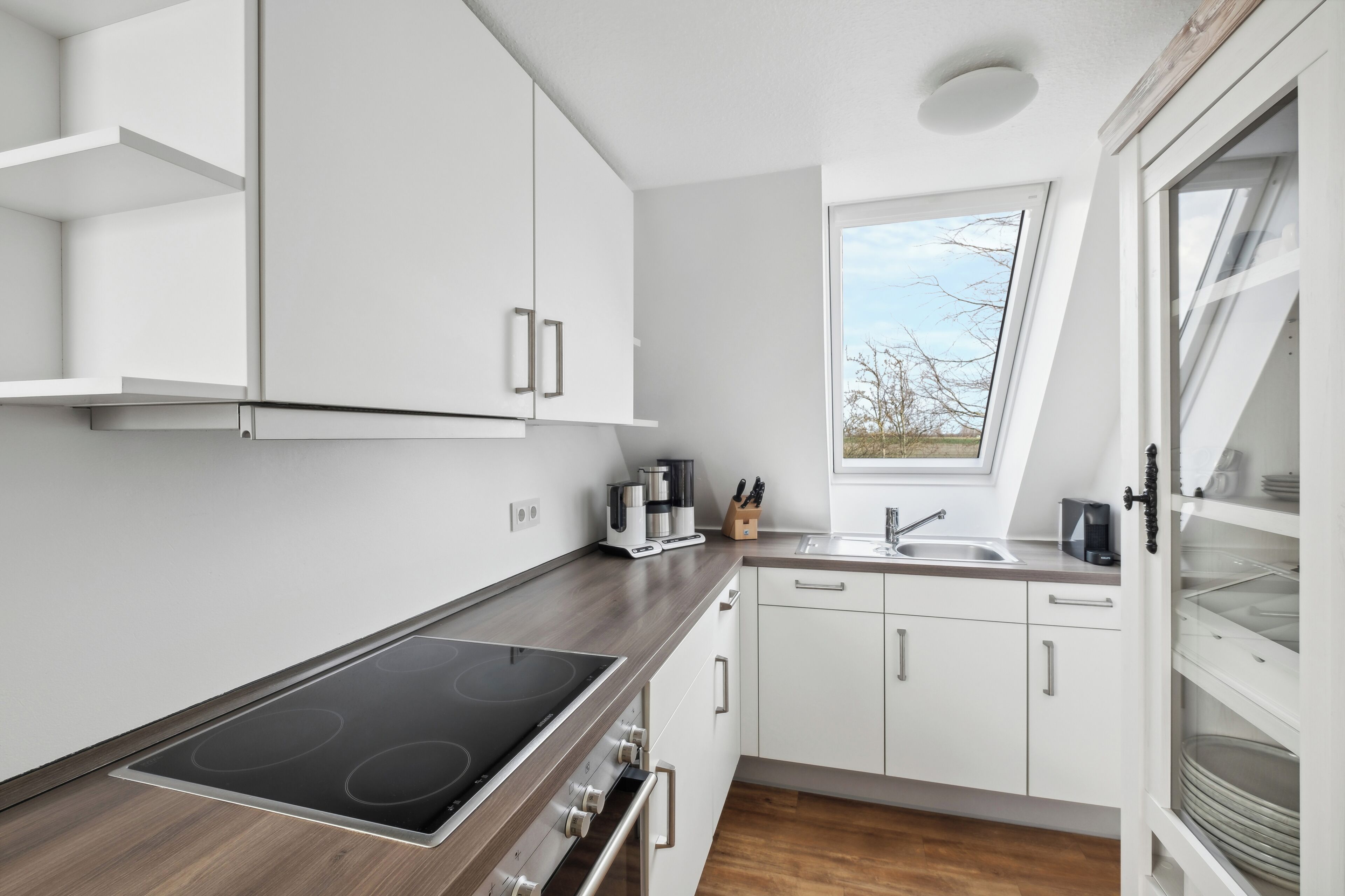 A modern kitchen with white cabinets, a built-in stove, and a window providing natural light.