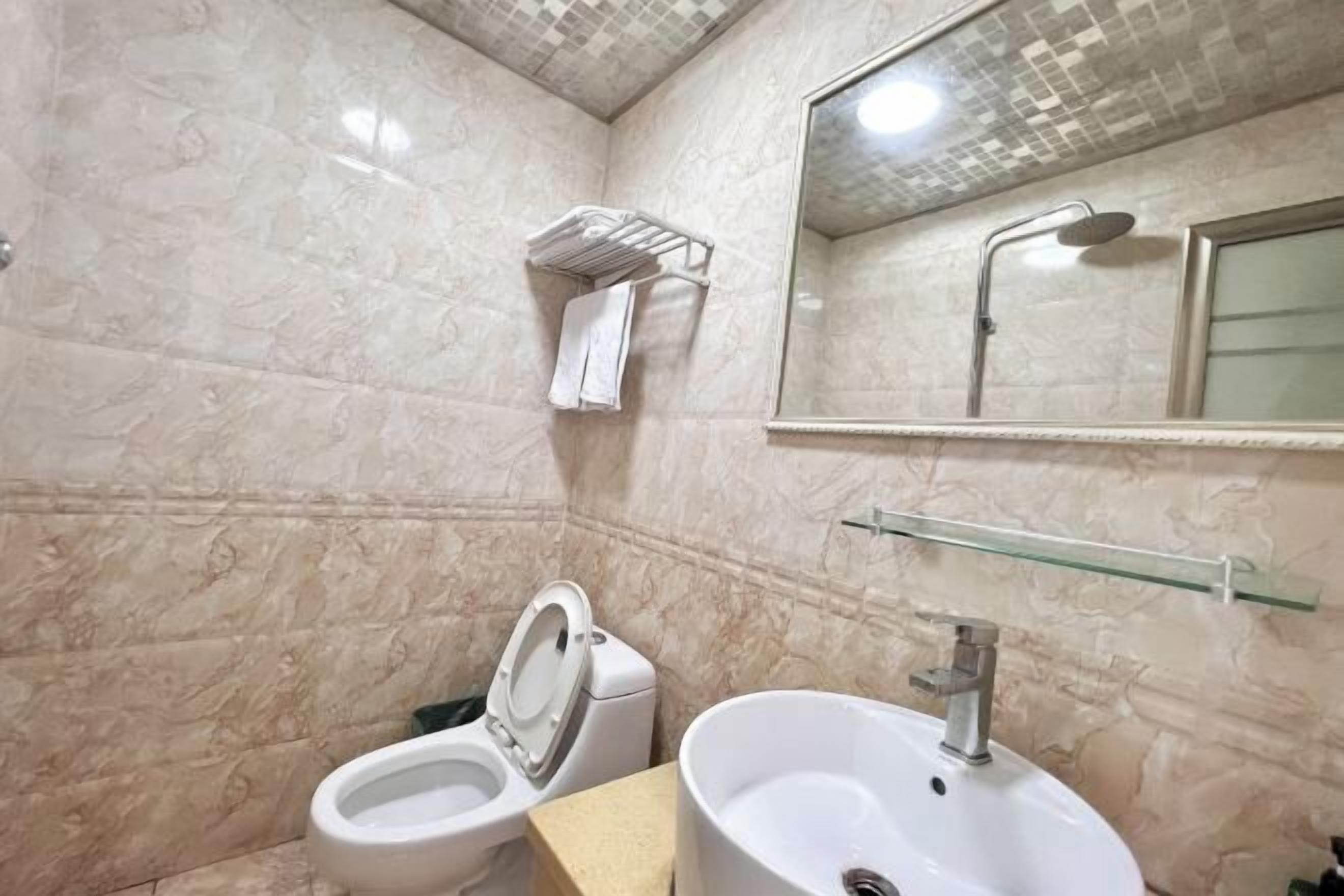 A bathroom with a toilet, sink, and a glass shelf.