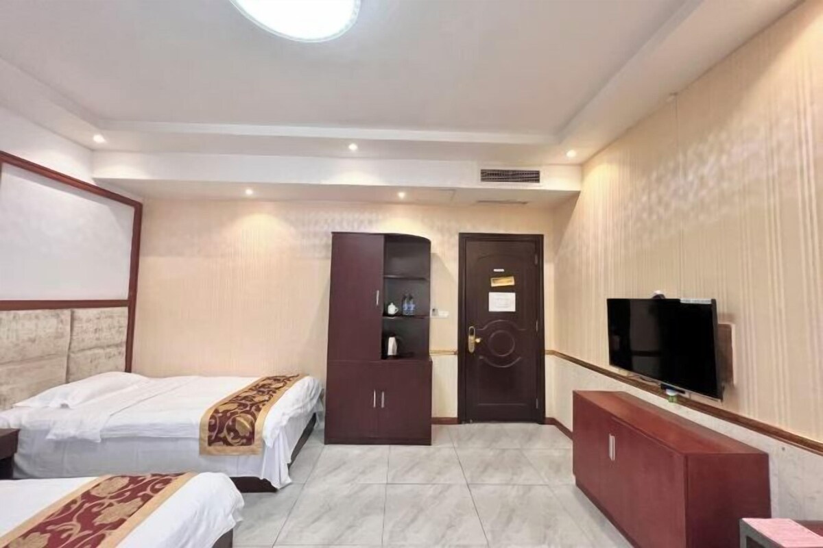 Habitación de hotel con dos camas, un armario, televisor y un escritorio pequeño.