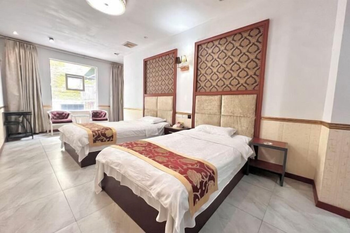 Habitación de hotel con dos camas, una mesita, una silla y un ventanal con cortinas.