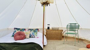 A tent with a bed, pillows, a green chair, a wicker basket, and a green blanket.