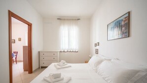 Ein Schlafzimmer mit zwei Betten, einem Nachttisch, einer Kommode, einem Fenster mit Vorhängen und einem Bild an der Wand.