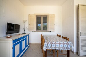 A compact kitchen with a TV, a table with chairs, a window with shutters, and a door.
