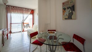 A dining area with a glass table and chairs, a white sofa, and a red patterned chair. - Ortensia House: tranquility and sea views in Selva di Fasano (Selva di Fasano)
