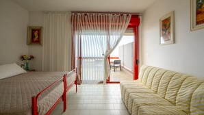 A bedroom with two beds, a sofa, a balcony with a chair, and a door leading outside. - Ortensia House: tranquility and sea views in Selva di Fasano (Selva di Fasano)
