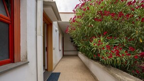 A narrow corridor with a tiled floor, a door on the left, and a planter with red flowers on the right. - Ortensia House: tranquility and sea views in Selva di Fasano (Selva di Fasano)