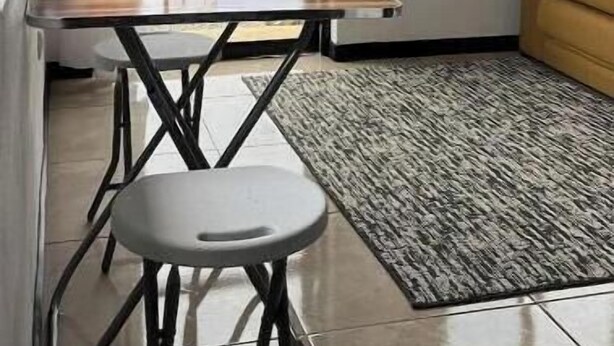 Una habitación con una mesa, una silla y un sofá. Se ve una ventana con vistas a aerogeneradores.