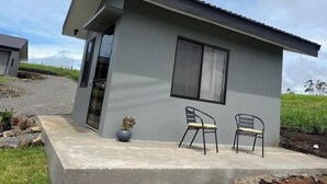 Un edificio moderno de una sola planta con techo plano, un ventanal grande y una puerta. En el patio de concreto hay dos sillas y una maceta.