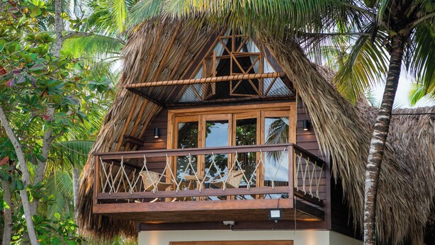 A thatched-roof bungalow with a wooden balcony, surrounded by tropical vegetation. - GAELIA BEACH (Santa Marta)
