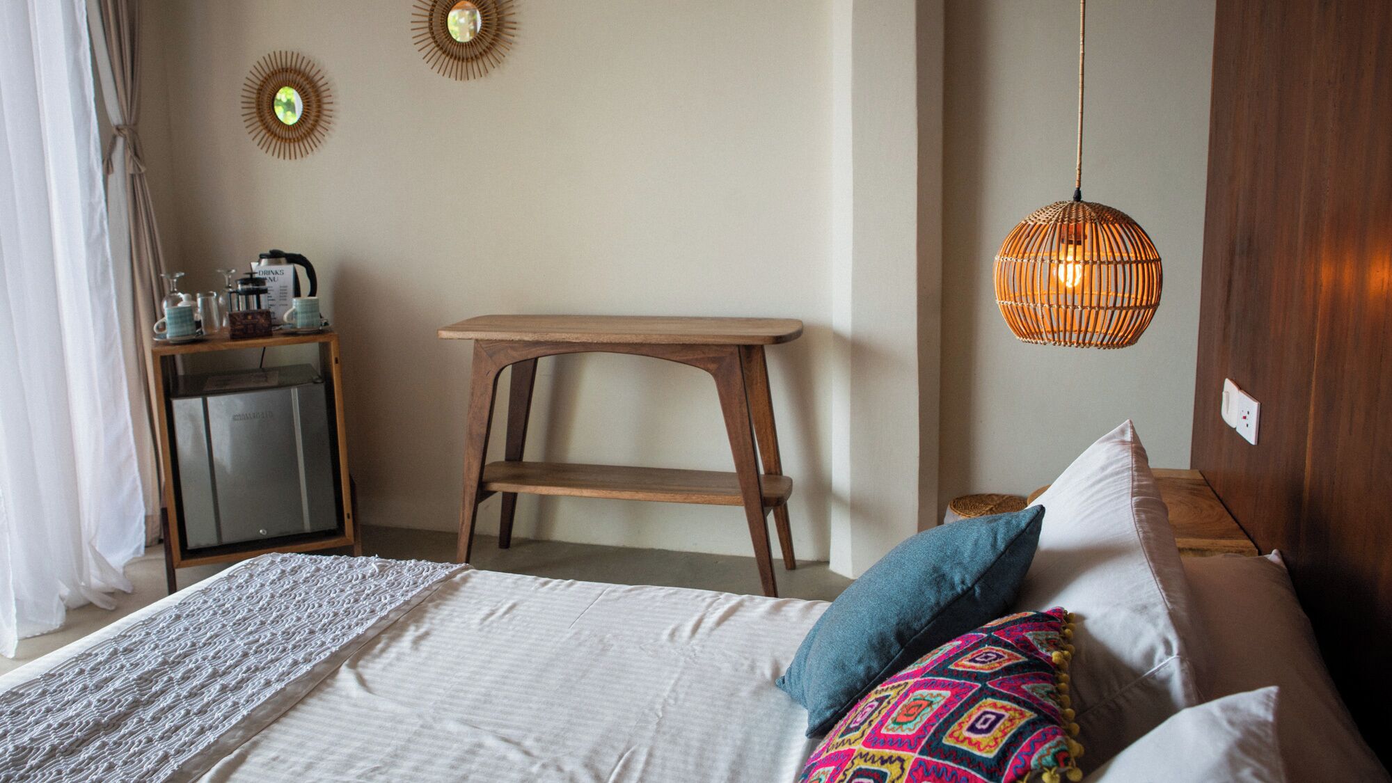 Une chambre à coucher comprenant un lit, des oreillers, une table de chevet, une petite armoire et un luminaire suspendu.
