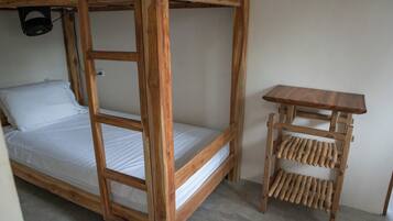 Een stapelbed met houten frame en witte beddengoed, een klein houten tafeltje met planken, en een plafondventilator.