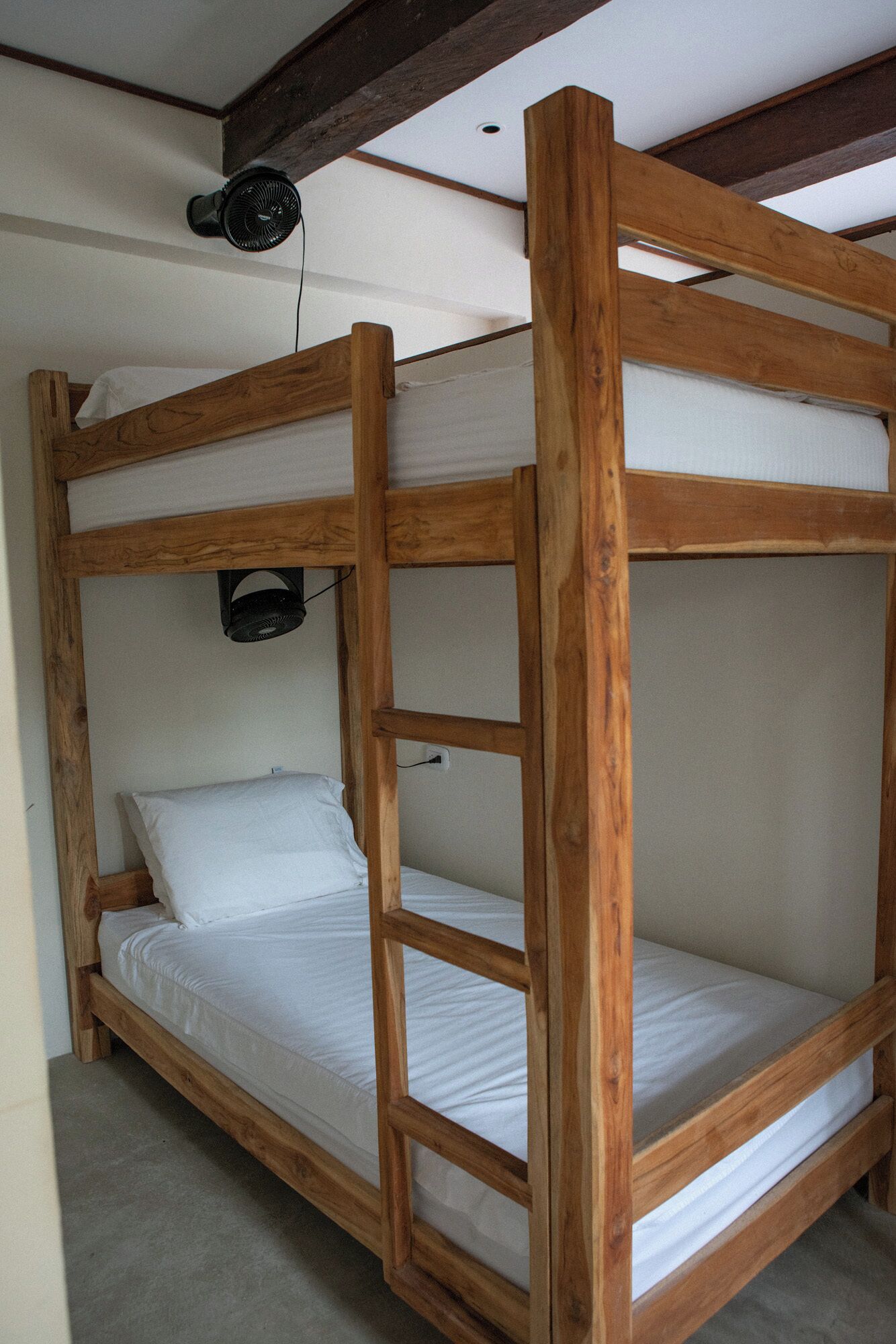 Una cama litera con estructura de madera, colchón blanco y ventilador de techo.