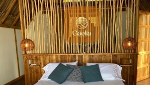 A bed with a wooden headboard, two decorative wall sconces, and a logo for Gæelia Beach. - GAELIA BEACH (Santa Marta)