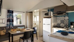 A compact kitchen with a microwave, stove, and refrigerator. There is a dining area with a table and chairs, and a window with curtains.