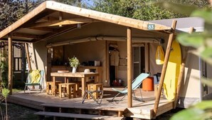 A wooden structure with a covered patio, numbered 83, featuring a table, chairs, and a surfboard.