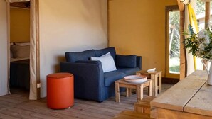 A cozy room with a dark blue sofa, a wooden table, a small orange stool, and a tent-like structure.
