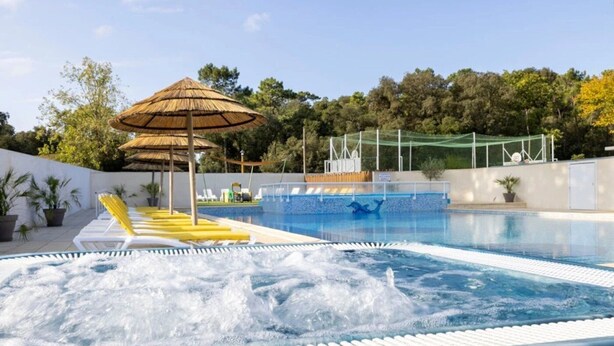 A swimming pool with hot tub, lounge chairs, and a shaded area with an umbrella.