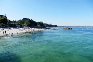 A beach with clear water, people swimming, and a rocky outcrop in the distance.