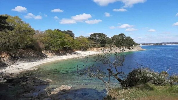 Paisaje costero con aguas azules cristalinas, playa arenosa y abundante vegetación.