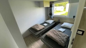 Una caravana pequeña y compacta, de una sola habitación, con dos camas, un ventanal y una kitchenette.