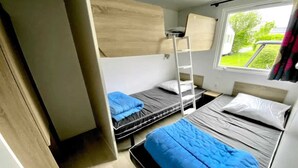 A compact room with bunk beds, a ladder, and a window with a view of greenery.