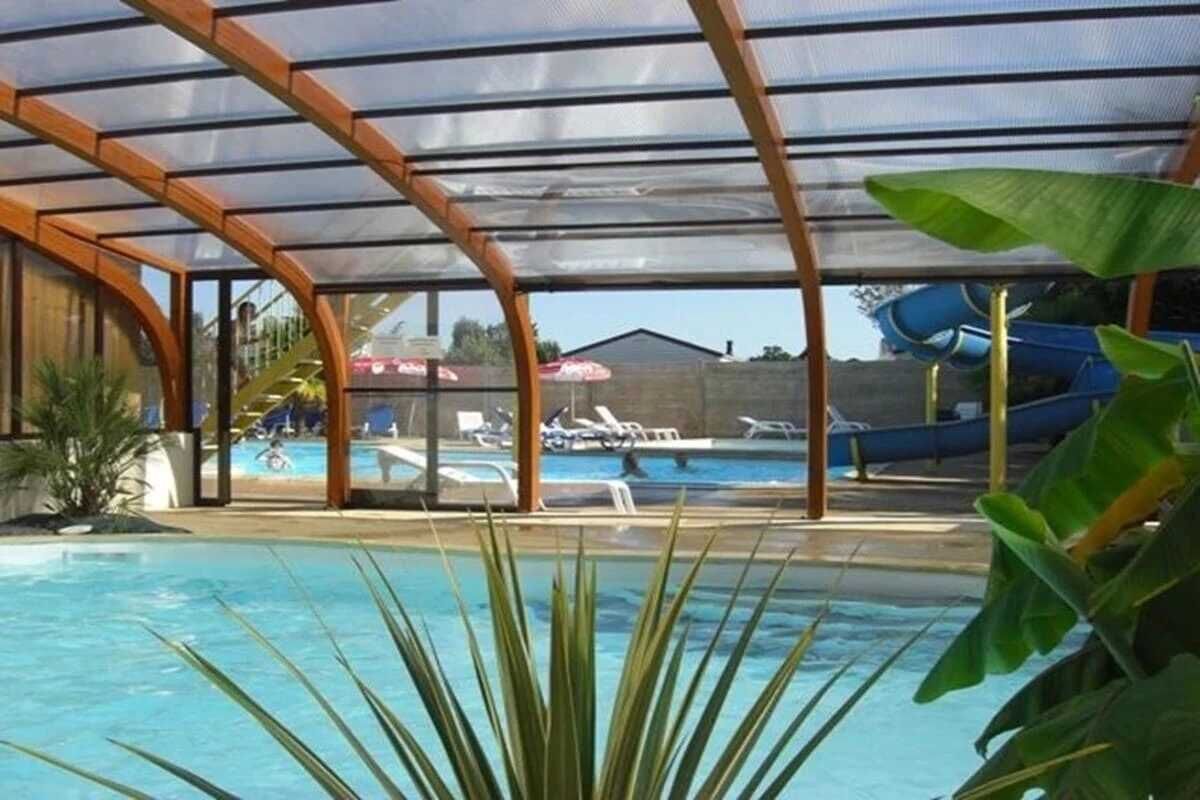Una piscina cubierta con techo transparente, rodeada de sillas de descanso y un tobogán.